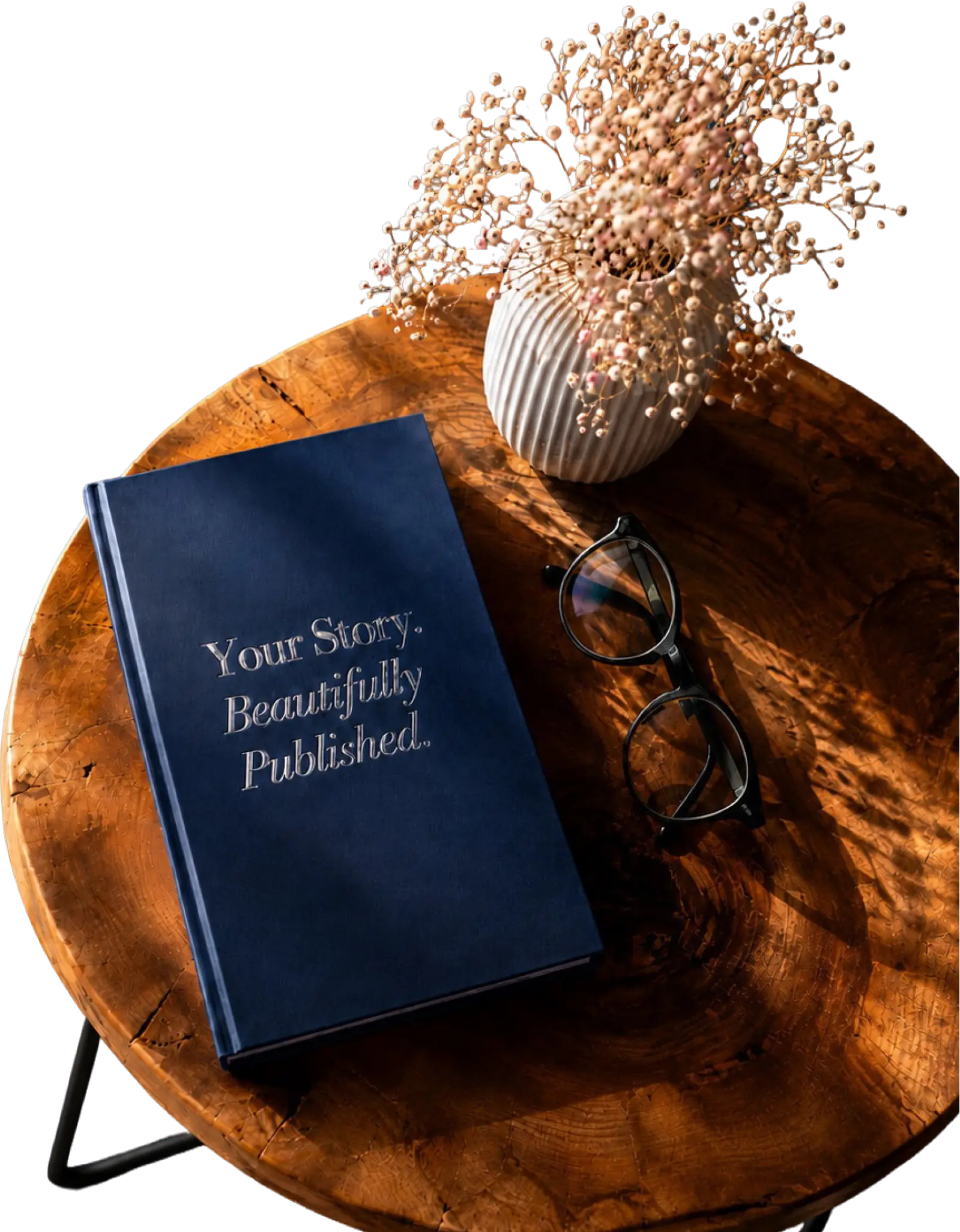 A navy hardcover book, glasses and flowers arranged on a wooden table